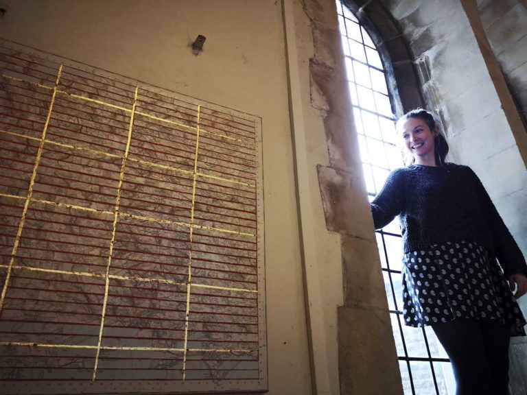 image of research fellow and project manager Chloe McKenzie at the window of Holy Trinity Chapel in Swansea installing the St Thomas Way exhibition Medieval and Modern Journeys